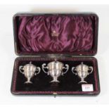 A late Victorian silver three piece cruet each in the form of a twin handled urn to include mustard,