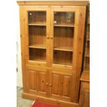 A modern pine side cupboard, having twin glazed upper doors, over twin recessed panelled lower