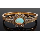 A yellow metal, opal and diamond hinged oval bangle, featuring a centre oval opal cabochon, having a