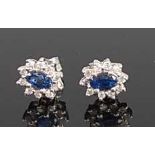 A pair of white metal, sapphire and diamond oval cluster earrings, each featuring a centre oval