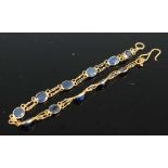 A yellow metal sapphire bracelet, having eleven oval faceted sapphires in bezel settings, with an
