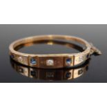 A late Victorian yellow metal, sapphire and diamond set hinge bangle, set with three round cut