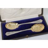 A cased pair of Edwardian silver serving spoons, each having shell shaped gilt-washed leaf and