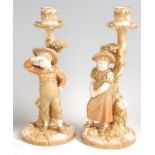 A pair of Hadley Worcester porcelain boy and girl candlestick figures, heightened in gilt, impressed