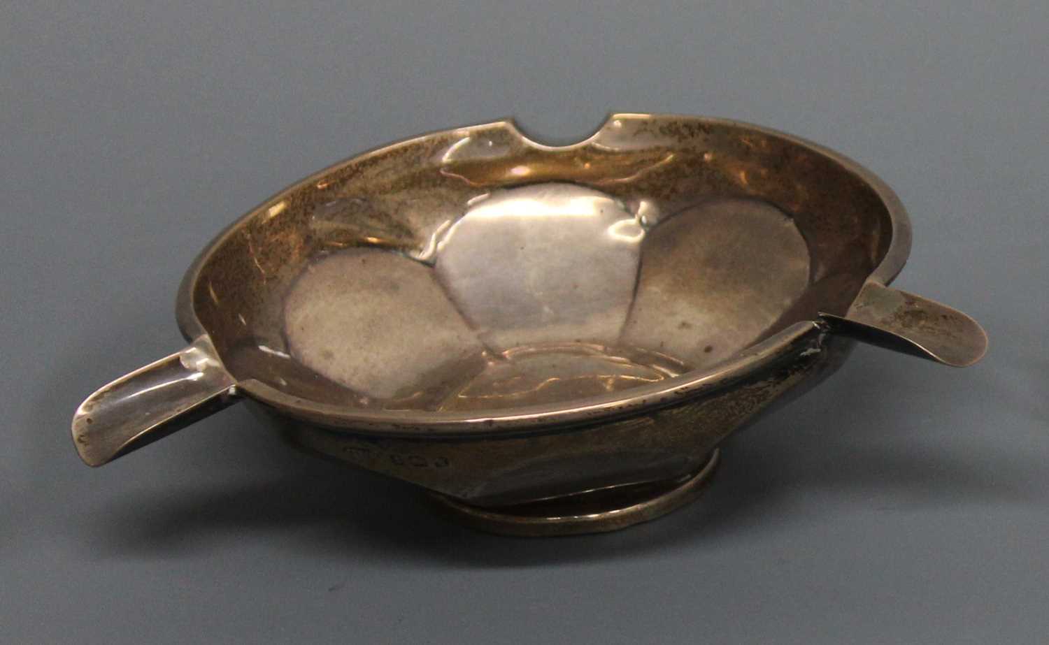 A late Art Deco silver circular ashtray, having pronounced cigarette rests to faceted plain circular
