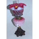 A Victorian oil lamp, having a frilled cranberry tinted vaseline glass shade above a pink glass font