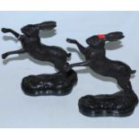 A pair of modern bronzed figures of boxing hares, each on a naturalistic base and marble plinth,