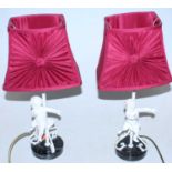 A pair of painted metal table lamps each surmounted by a cherub on marble base with pleated silk