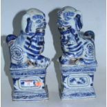 A pair of reproduction blue & white glazed temple dogs, in seated pose on rectangular plinths,