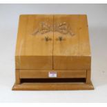 An early 20th century pine table-top stationery cabinet, the hinged sloping front carved with a bow,