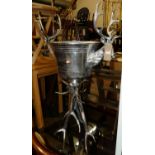 A large polished chromed metal freestanding ice bucket, having stag head handles, raised on