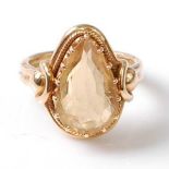 A yellow metal citrine dress ring, featuring a pear cut citrine in a claw setting, with stirrup