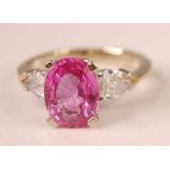 A white metal, pink sapphire and diamond three stone ring, featuring a centre oval faceted pink