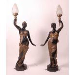 A pair of bronzed metal figurines of maidens, each holding aloft a flaming torch, in black and gilt,