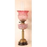 A Victorian pedestal oil lamp, having a cranberry tinted acid etched shade, over a polychrome