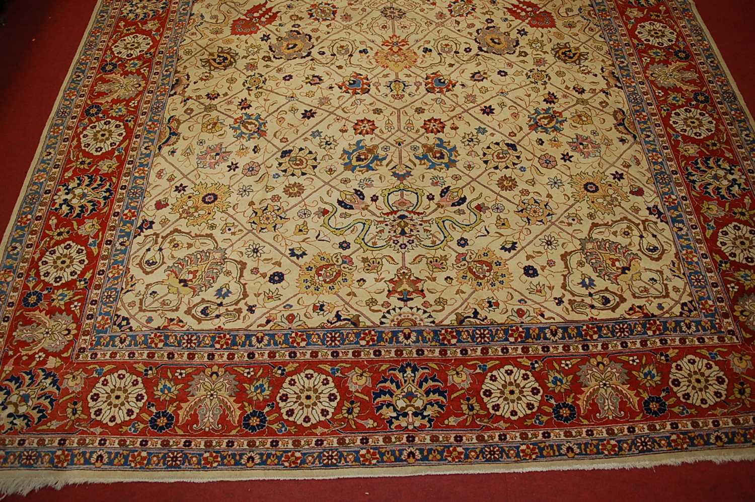 A Persian woollen cream ground carpet, decorated with scroll flowers and foliage within trailing