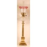 A lacquered brass pedestal oil lamp, having a crinoline cranberry glass and repousee decorated