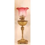 An Art Nouveau gilt metal pedestal oil lamp, having a cranberry tinted and plain acid etched moulded