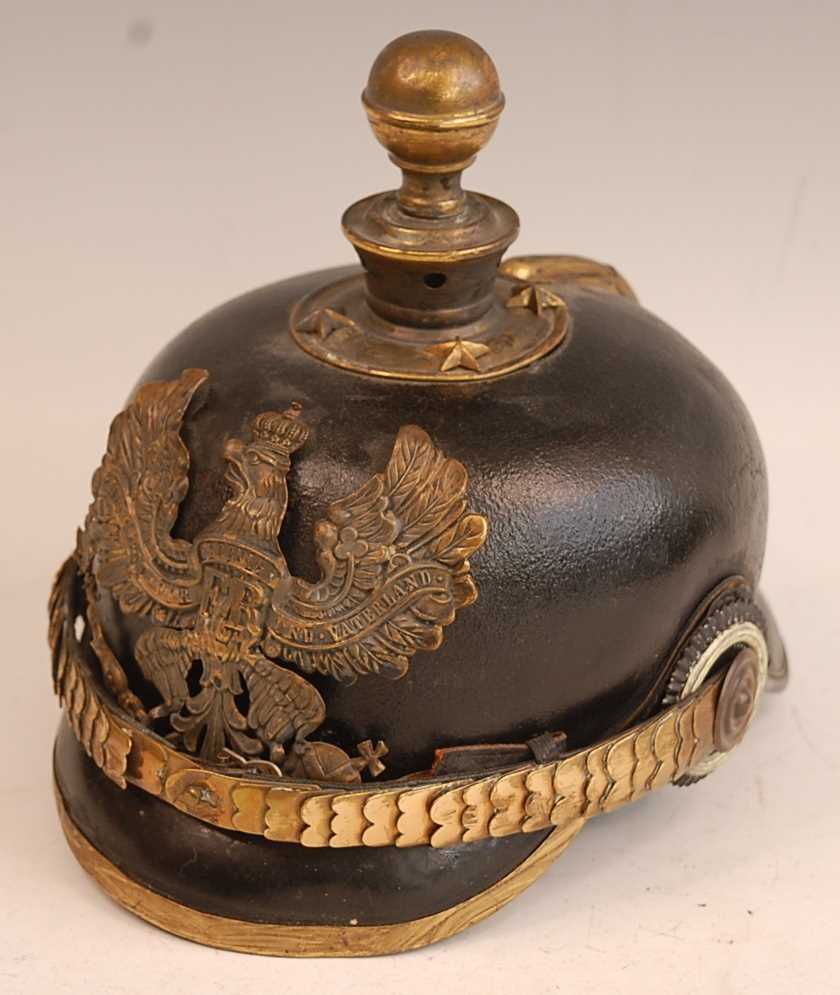 A Prussian pickelhaube, the leather skull with brass ball top and eagle plate, flanked by state