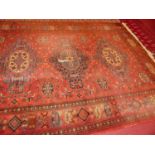 A Persian style machine woven red ground Bokhara rug (worn section to centre, and fading to colours)