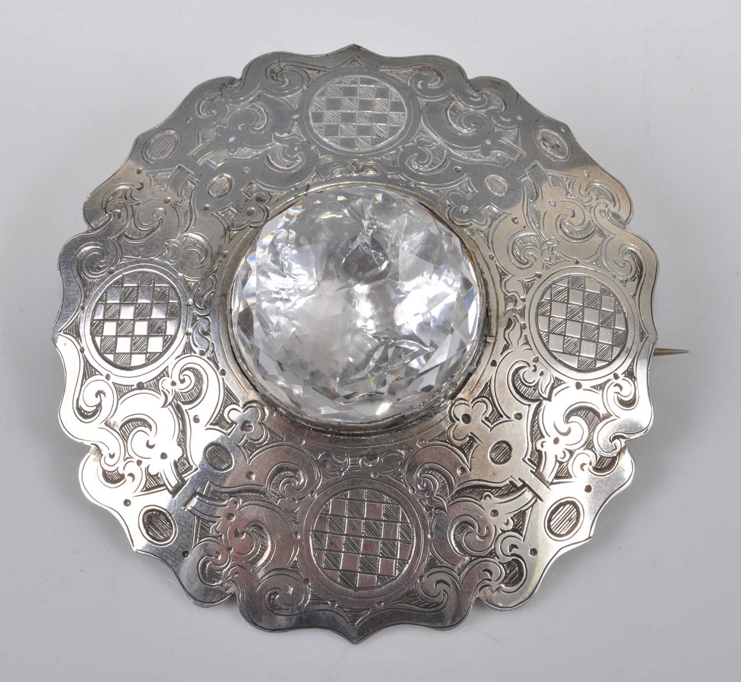 A white metal large circular Celtic brooch, engraved with scrollwork and chequerboard pattern,