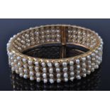 A yellow metal and cultured pearl set hinged bangle, arranged as four rows of small pearls in fine