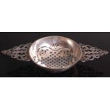 A George II silver twin-handled lemon strainer, having decoratively pierced bowl and scrolling