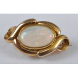 A yellow metal opal brooch, featuring an oval opal cabochon bezel set within a scrollwork