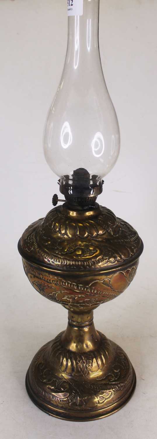 An Art Nouveau influenced embossed brass floral decorated oil lamp, with glass chimney, height 53.