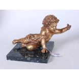 A gilt painted model of a cherub in reclining pose with outstretched arm, on a square marble base,
