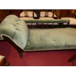 An Edwardian ebonised and blue Dralon buttoned upholstered chaise longue, raised on turned supports,