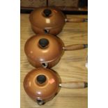 A graduated set of three brown enamelled Le Creuset saucepans and covers