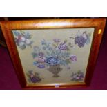 A framed woolwork panel depicting an urn issuing flowers, 43x43cm, in glazed frame, together with an