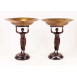 A pair of tazza, each having a brass bowl supported by a bronzed figure of a maiden with arms aloft,