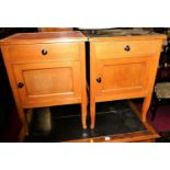 A pair of faded beech single door bedside cupboards, each with single upper drawers (one lacking