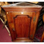 An early 19th century oak single door hanging corner cupboard