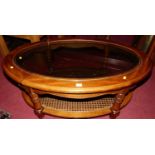 A contemporary hardwood and smoky glass inset oval two-tier coffee table, length 107cm; together