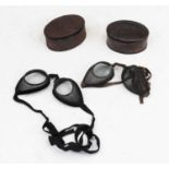 A pair of WWI period goggles each having oval lenses within mesh surround on the fabric strap on