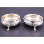 A pair of Victorian silver salt cellars, decorated in a blossom pattern and having scroll feet, G