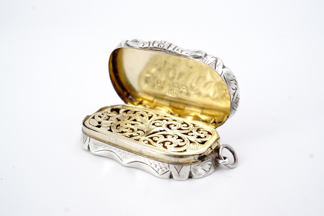 A Victorian silver fob vinaigrette, of oval section with a cusped rim and engraved sides, the covers