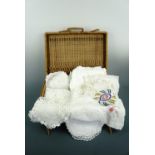A rattan case containing antique and vintage table linens and textiles, including table cloths,