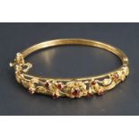 A garnet and 9ct gold hinged bangle, the outer face an elliptical arrangement of two bars framing