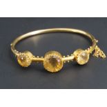 A Victorian citrine and yellow metal hinged bangle, comprising three large circular cut gems, the