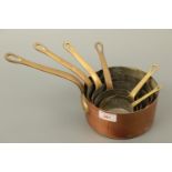 A graduated set of copper and brass sauce pans, largest 16 cm diameter, smallest 7 cm