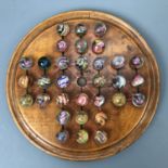 A 19th Century turned wooden solitaire board and glass marbles