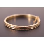 A 9ct gold hinged bangle, decorated with wriggle work and facet cutting, 5.8 cm internal diameter,