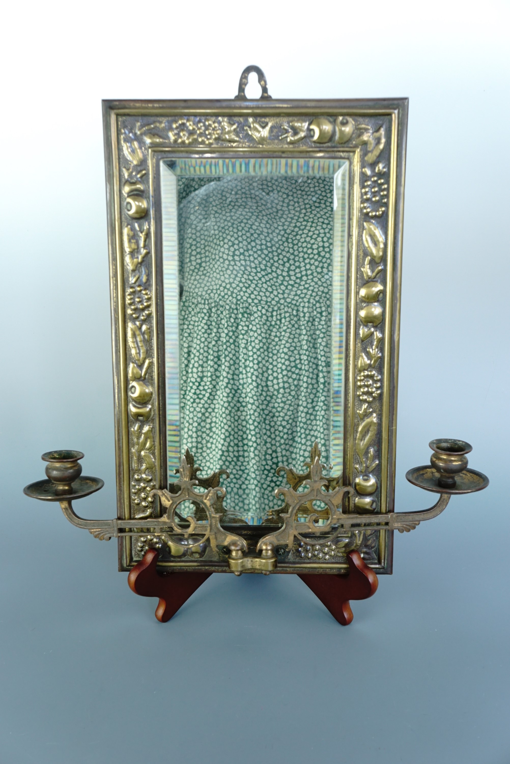 An antique brass framed two-branch candle sconce, bearing repousse decoration in the form of fruit