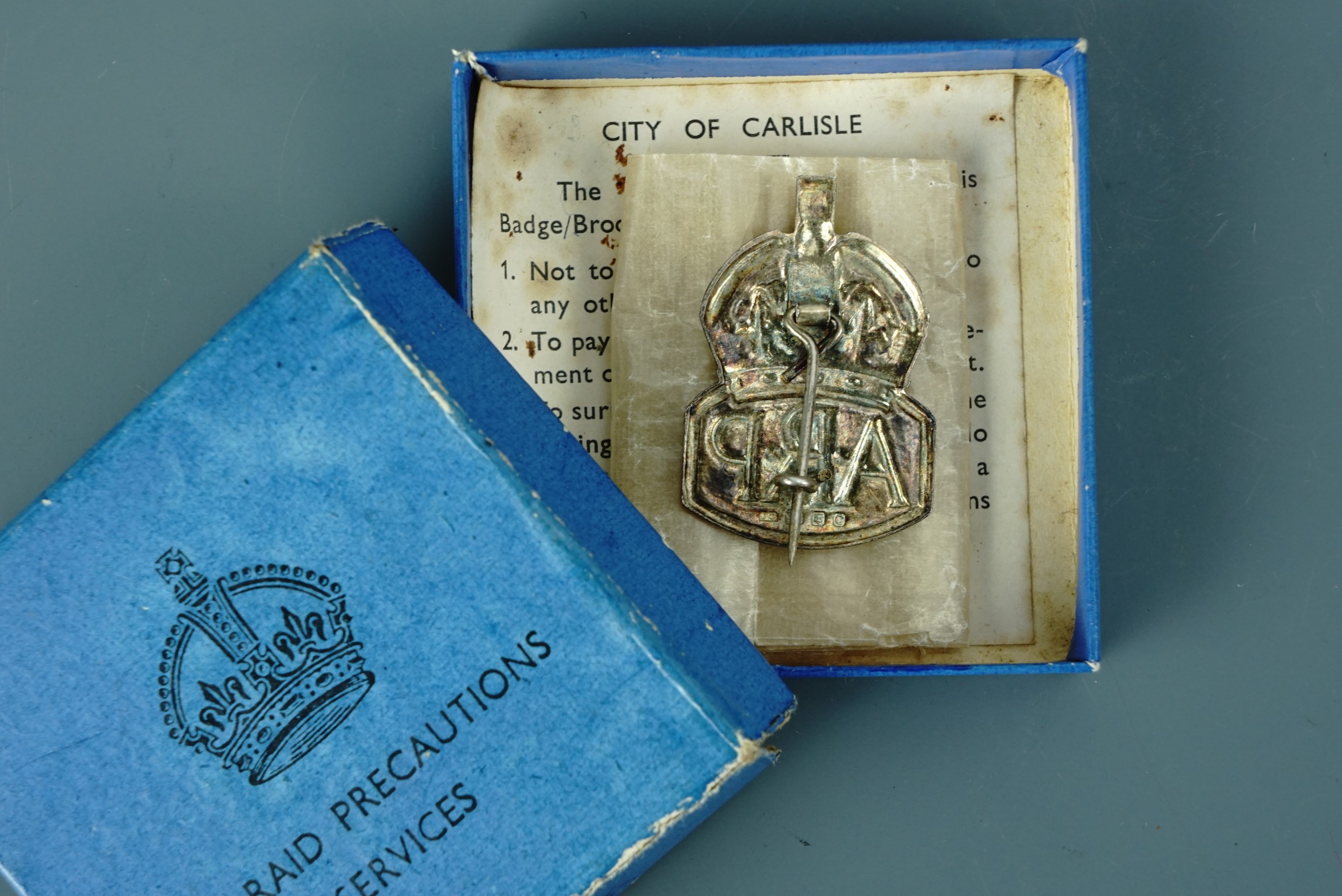 A Second World War silver ARP badge in carton with City of Carlisle ARP Department printed