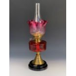 A Victorian oil lamp, having a cranberry glass reservoir and etched achromatising shade, 43 cm to