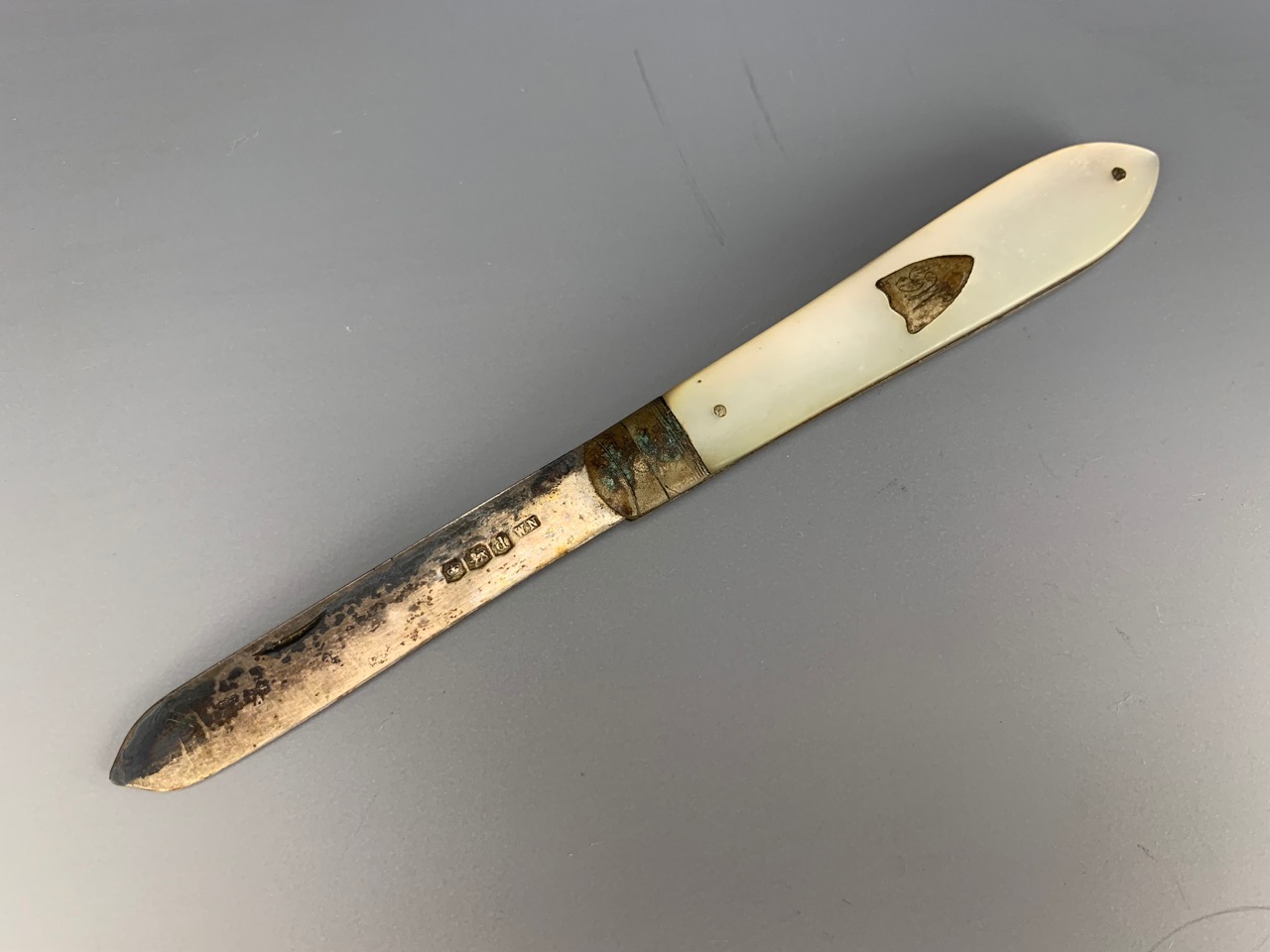 A silver pocket folding fruit knife, one mother-of-pearl grip scale inset with a shield-shaped